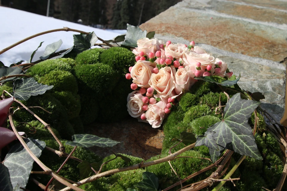 Ein Urnenkranz mit blassrosa Rosen, kleinen Beeren und Moos.